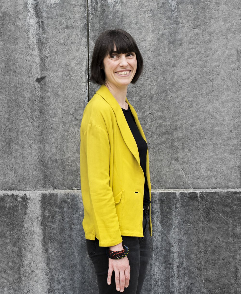 Portrait of Éléonore Lépinard against a concrete wall, wearing a yellow blazer